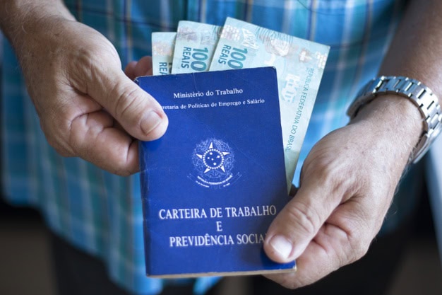 Pessoa segura carteira de trabalho, em fotografia ilustrativa